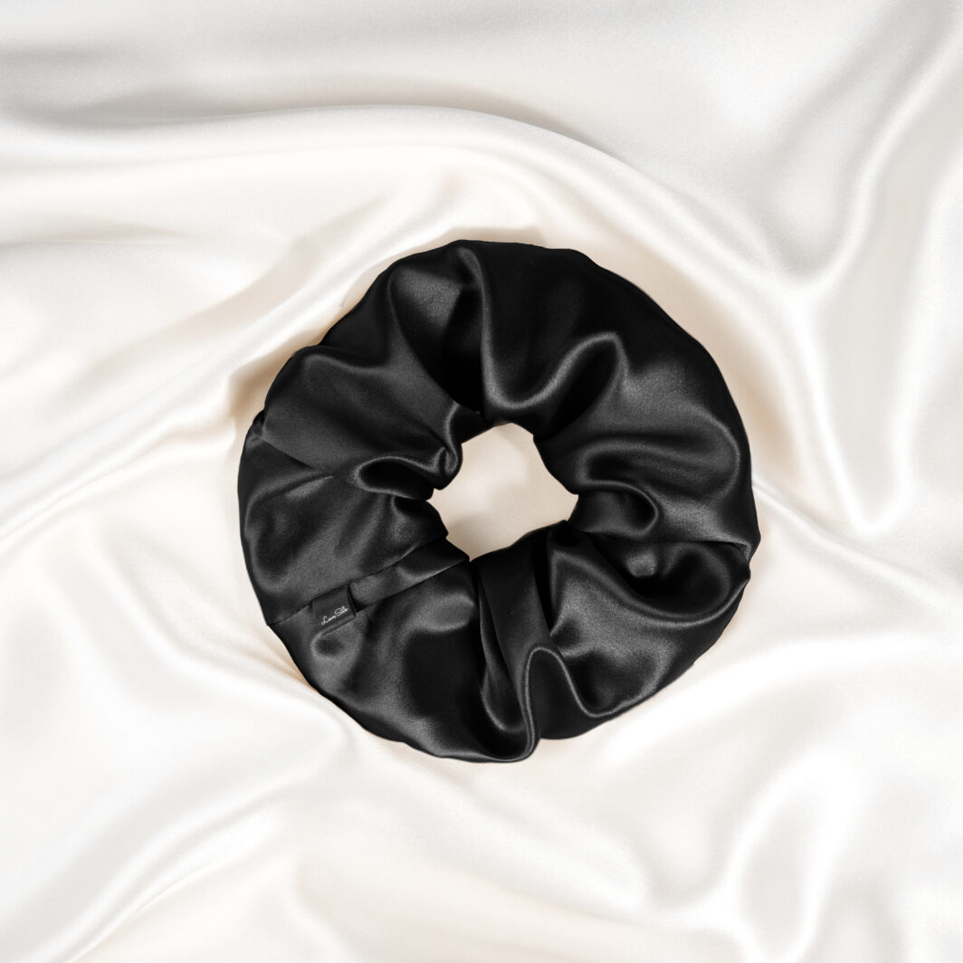 Luxuriöser schwarzer Seidenschal als Haargummi auf seidigem Stoff Hintergrund, hochqualitative Seidenaccessoires von Lovesilk.
